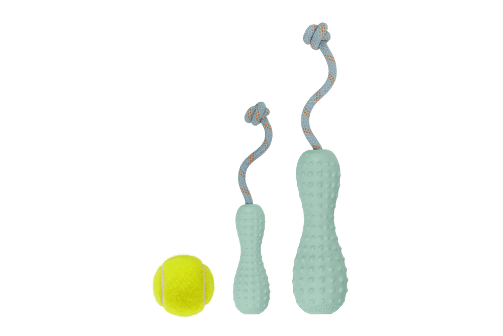 Zwei grüne Gummi-Wurfspielzeuge in Flaschenform mit Noppen und Schlaufen, neben einem gelben Tennisball.