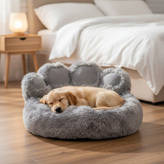 Schlafender Welpe in grauem, runden Hundebett in Pfotenform mit weichen Rändern auf einem gemütlichen Hintergrund.