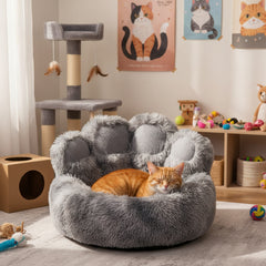 Gemütliches graues Katzenbett in Pfotenform mit entspannter orangefarbener Katze, umgeben von Kratzbaum und Spielsachen.