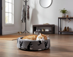 Gemütliche runde Plüschbett für Katzen in Grau mit schwarzen Motiven, orangefarbene Katze schläft darin.