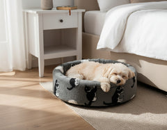 Kleiner Hund entspannt in grauem Plüschbett mit Katzenmotiven in einem modernen Schlafzimmer.