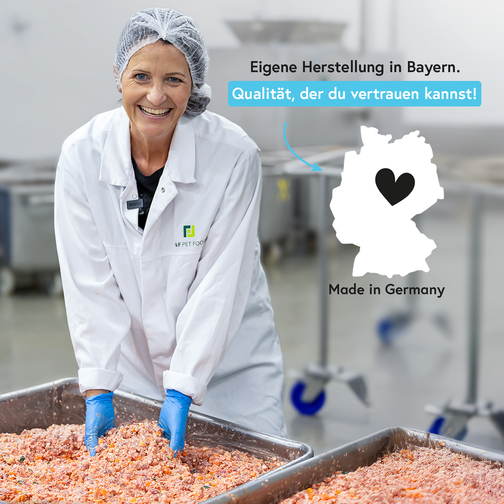 Lächelnde Frau im Labormantel bei der Fleischzubereitung in einer Produktionsumgebung.