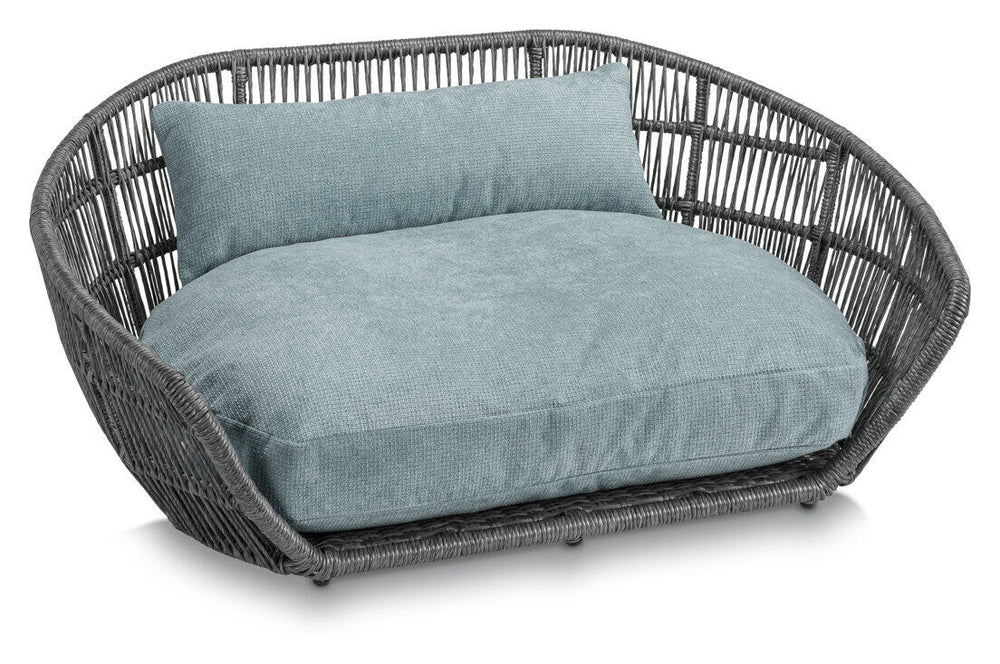 Elegantes ovales Hundebett TUDOR aus grauem Rattan mit hellblauem Kissen für einen stilvollen Schlafplatz.