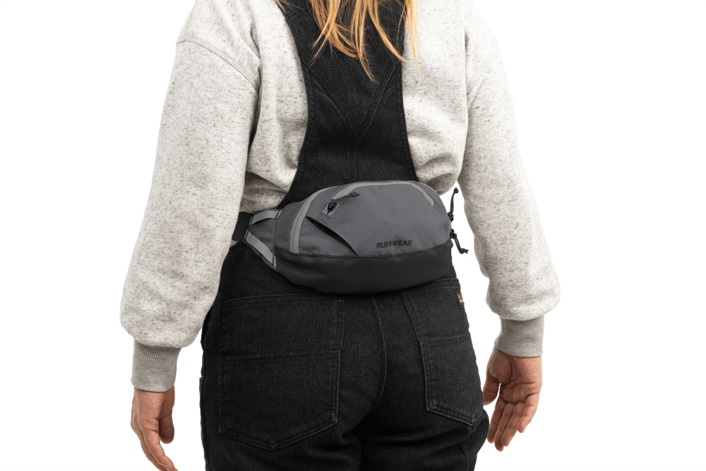 Person trägt graue Home Trail™ Hüfttasche über dem Rücken, ergänzt durch einen grauen Pullover.