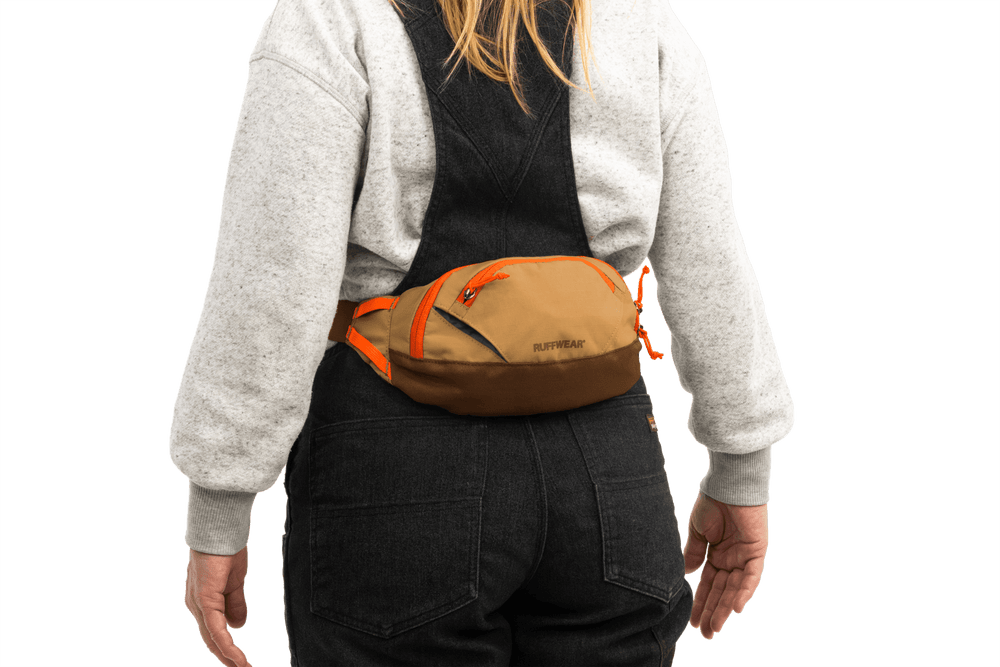 Person von hinten mit brauner Home Trail™ Hüfttasche und orangefarbenen Akzenten, grauem Pullover und schwarzen Leggings.