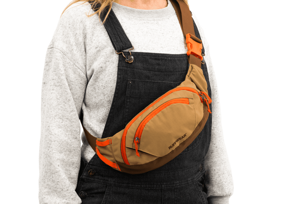 Person mit brauner Home Trail™ Hüfttasche und orangefarbenen Akzenten, in grauem Pullover und schwarzer Hose.
