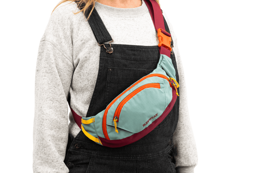 Person mit mintgrüner Hüfttasche und bunten Akzenten trägt graues Sweatshirt. Ideale Begleitung für Outdoor-Aktivitäten.