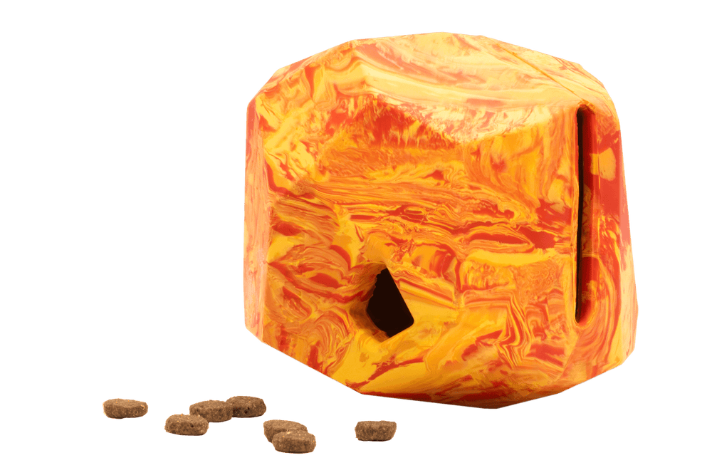 "Farbiger, marbelierter Futterspender in polyedraler Form, umgeben von Trockenfutter in Orange und Gelb."