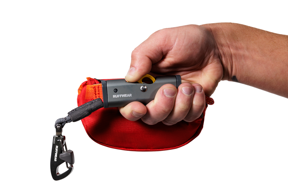 Hitch Hiker™ Hundeleinenhalter in der Hand, mit roter Tasche und Karabiner, ideal für unterwegs.