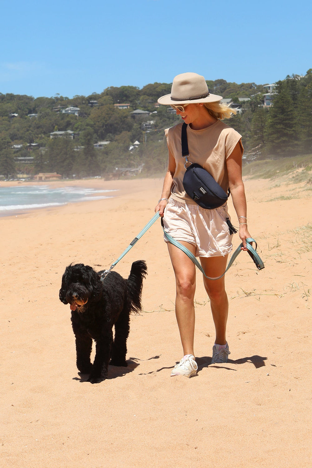 Frau am Strand mit schwarzem Hund an DOOG Neoprene Hundeleine, trägt beigen Hut und lässige Kleidung.