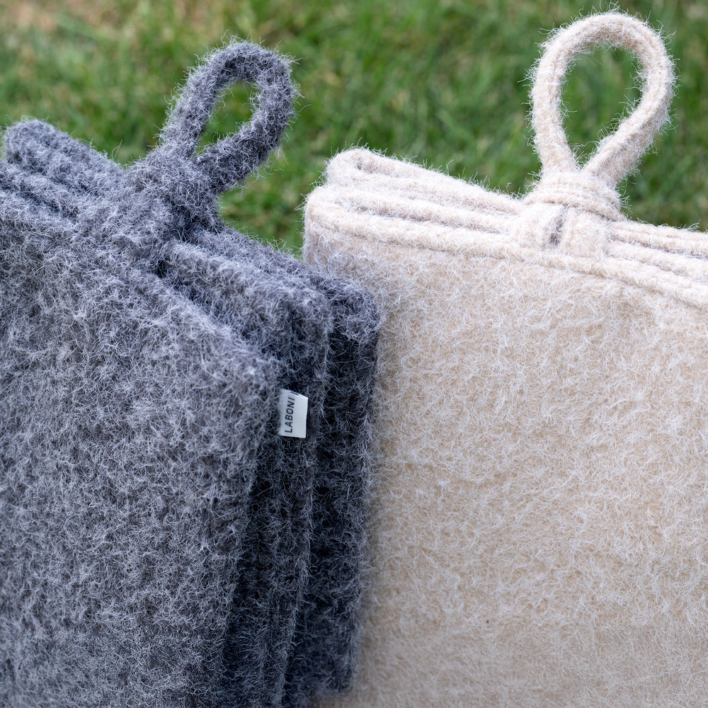 Stapelbare gefilzte Reisedecke Pads in grau und beige mit praktischen Schlaufen auf einer grünen Wiese.