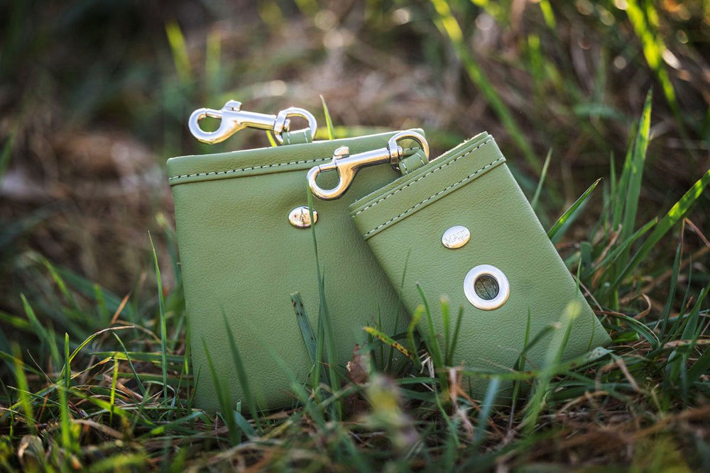 Zwei grüne Lederbörsen mit Clipverschluss und goldenen Knopfdetails liegen im Gras.