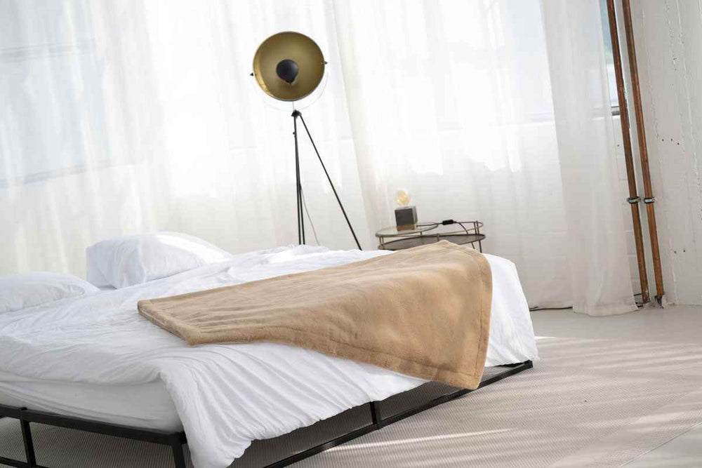 Hell eingerichtetes Schlafzimmer mit weißem Bett und beiger Wohndecke aus Webpelz. Moderne Stehlampe ergänzt den Raum.