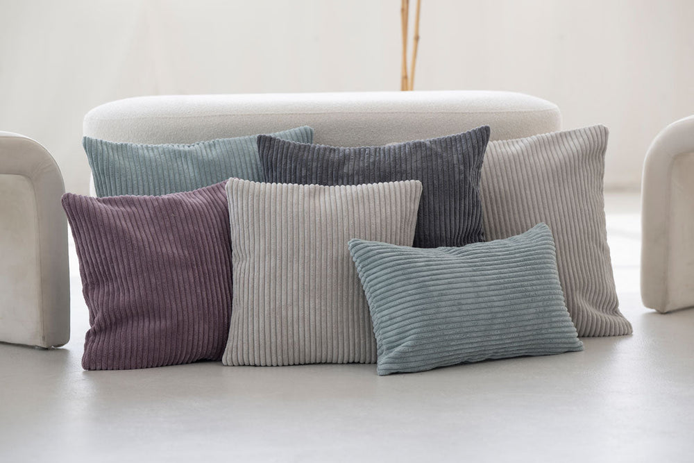 Bunte Kissenbezüge aus Cord in verschiedenen Farben und Texturen auf hellem Hintergrund angeordnet.