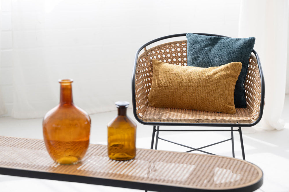 Moderne Kissenbezüge in Dunkelblau und Goldbraun auf einem Rattanstuhl mit schwarzem Metallgestell.