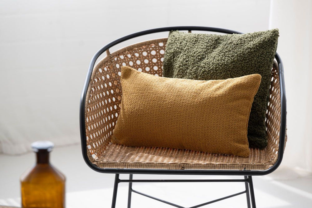Moderner Stuhl mit Rattan-Sitz und zwei Kissen in olivgrün und senfgelb, dekoriert mit einer stilvollen Atmosphäre.