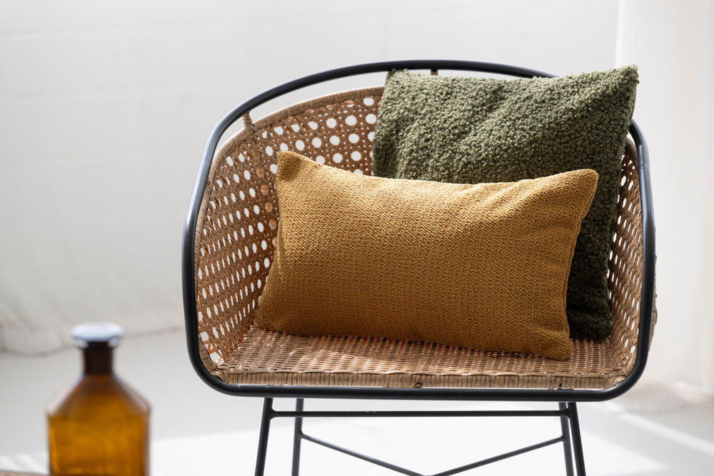 Moderner Stuhl mit Rattan-Sitz und zwei Kissen in olivgrün und senfgelb, dekoriert mit einer stilvollen Atmosphäre.