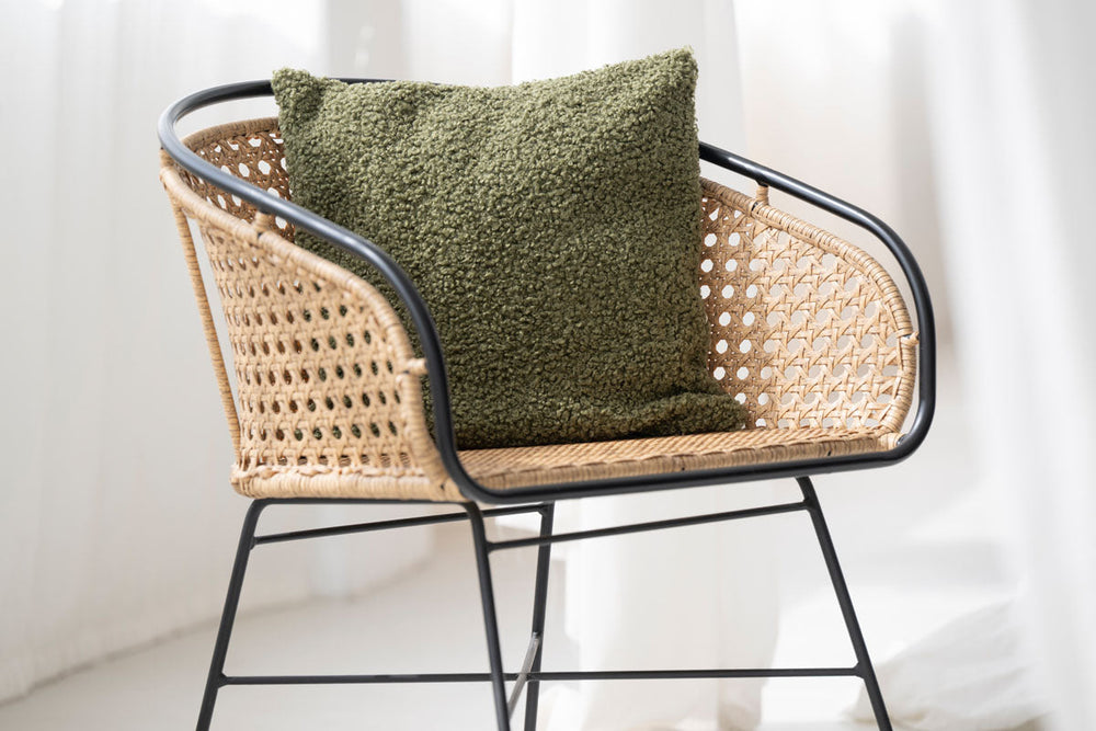 Kuscheliger olivgrüner Kissenbezug auf modernem Stuhl mit geflochtenem Korbdesign und schwarzem Metallgestell.