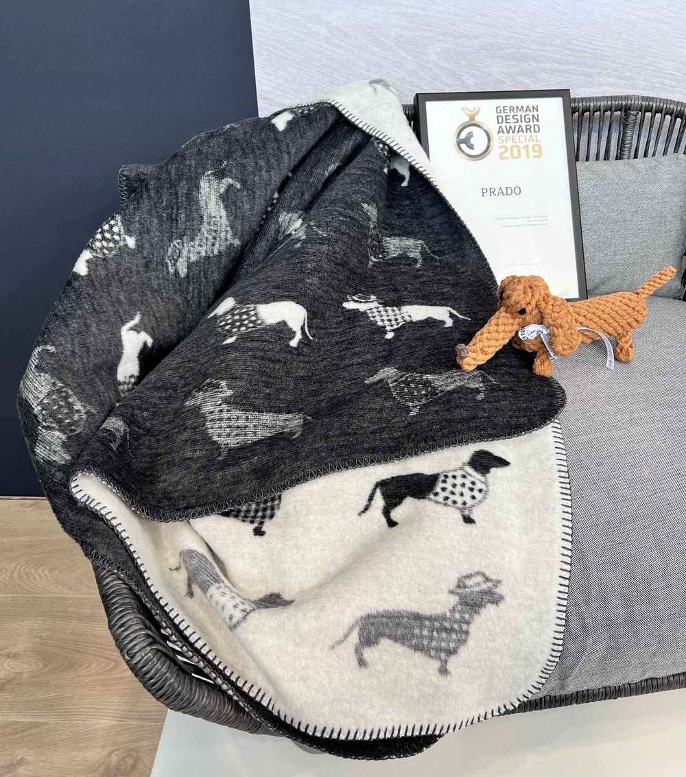 Wendedecke TECKEL mit Dackelmotiv auf Sessel, dekoriert mit Hundespielzeug in Braun und stilvollen Grautönen.