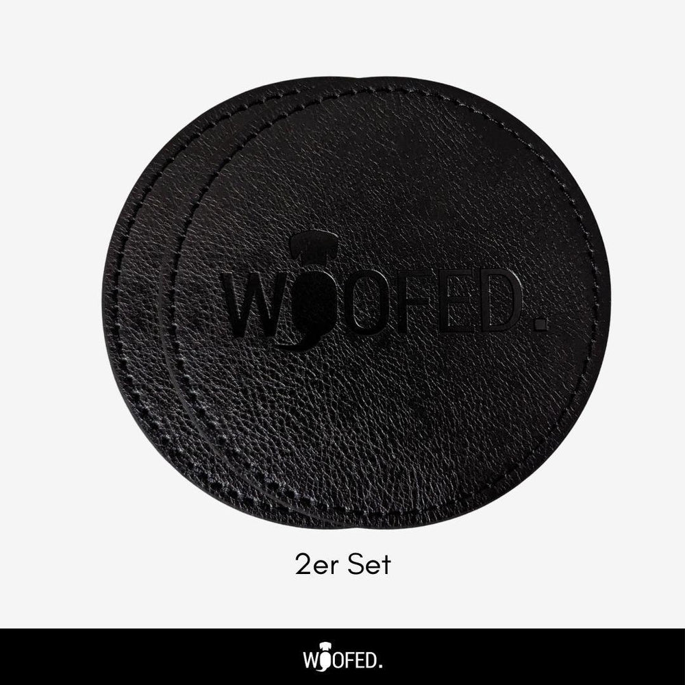 Schwarzes Leder-Set mit zwei runden Getränkeuntersetzern, eingeprägt mit dem Logo "WOOFED".