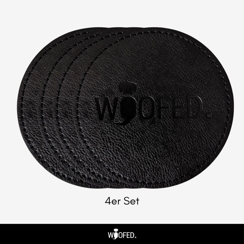 Schwarzes Leder-Set mit vier runden Getränkeuntersetzern und eingestanztem "WOOFED"-Logo.