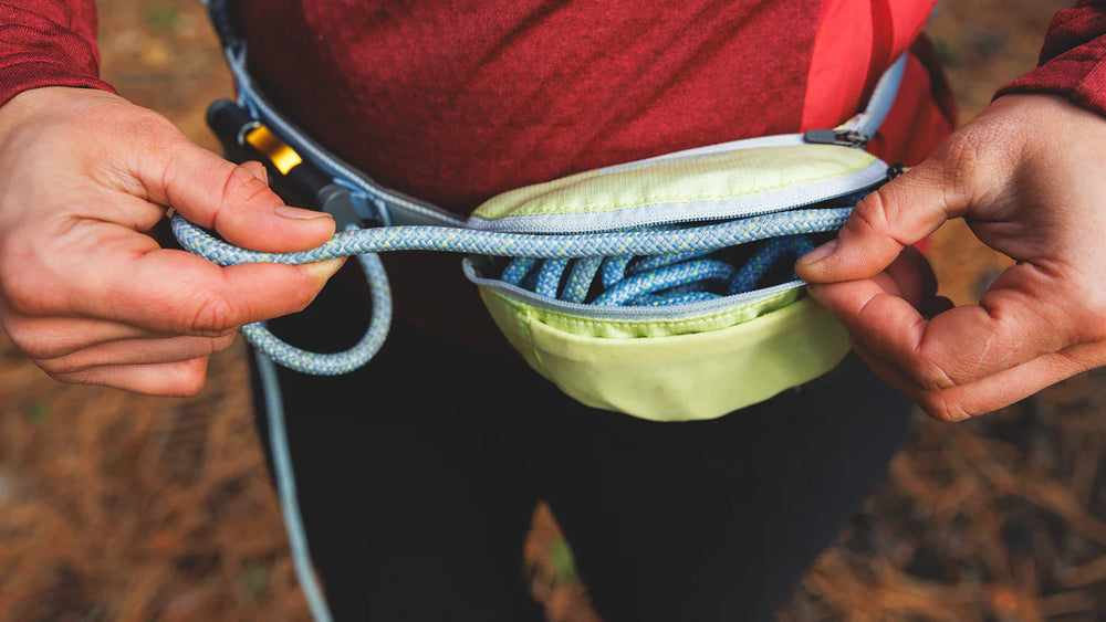 Person hält strapazierfähige Gürteltasche mit blau-weissem Seil, während sie ein rotes Oberteil trägt.