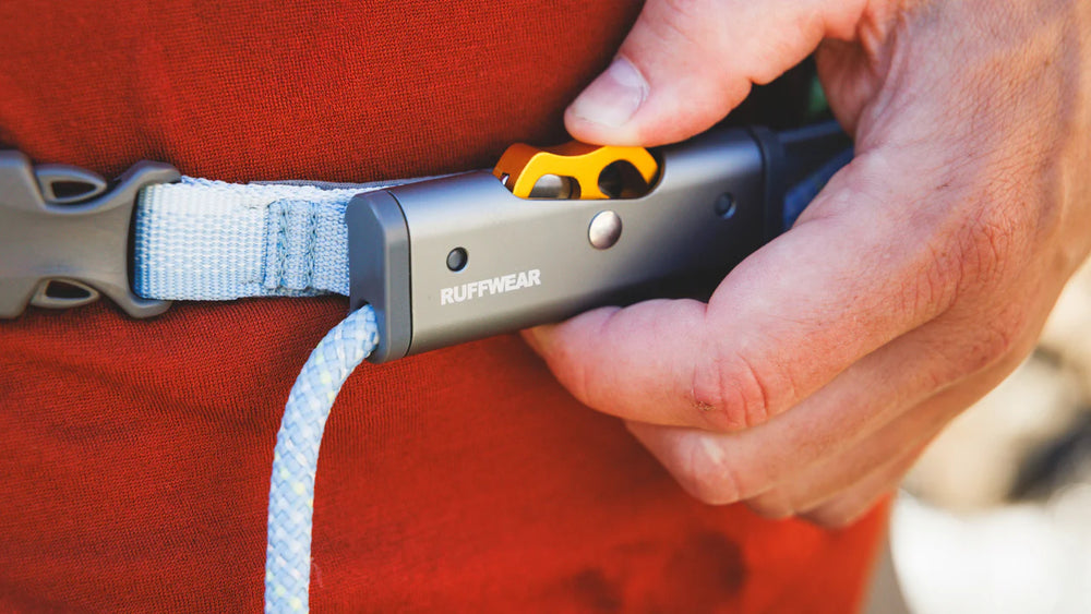 Hand betätigt silbernen Verschluss mit orangefarbenem Hebel des Hitch Hiker™ Leinensystems von Ruffwear.