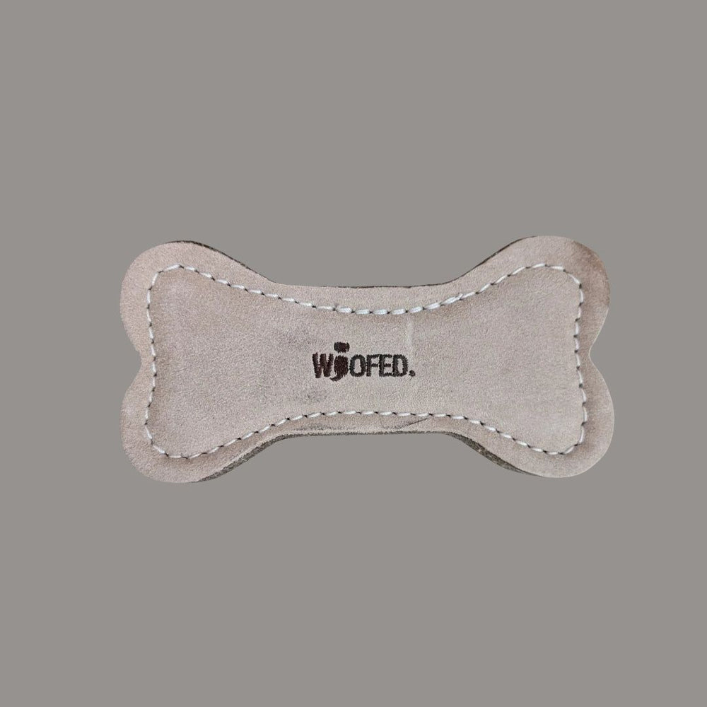 Natürliches Hundespielzeug in Knochenform mit weicher Oberfläche und gesticktem "WOOFED." Schriftzug. Ideal für spielende Hunde.
