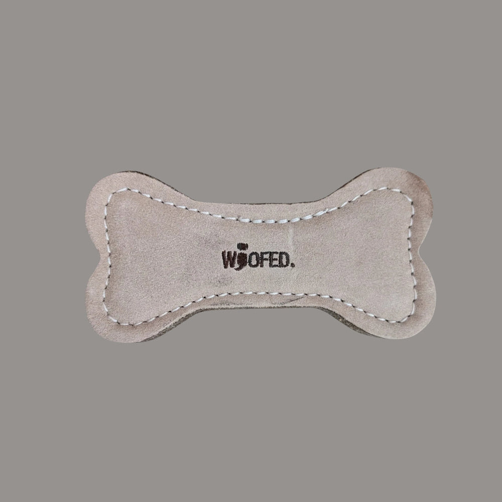 Natürliches Hundespielzeug in Knochenform mit weicher Oberfläche und gesticktem "WOOFED." Schriftzug. Ideal für spielende Hunde.