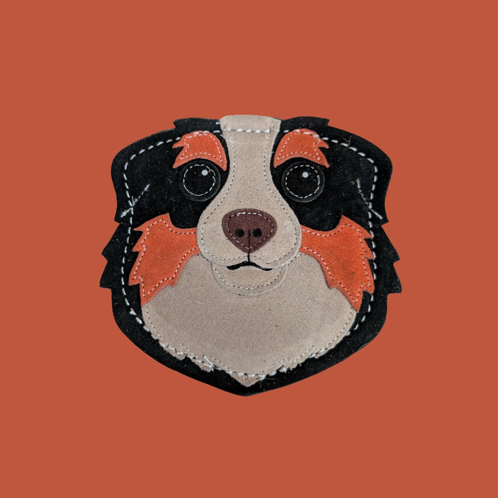 Natürliches Hundespielzeug in Form eines Hundekopfes aus Leder mit braunen und schwarzen Farbtönen und großen Augen.