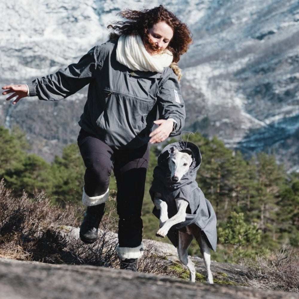 Frau und Hund in grauen Jacken beim Winterspaziergang in schneebedeckter Berglandschaft mit Hundejacke Expedition Parka.