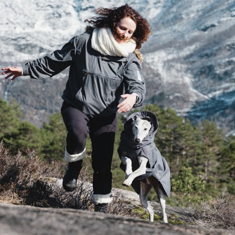 Frau und Hund in grauen Jacken beim Winterspaziergang in schneebedeckter Berglandschaft mit Hundejacke Expedition Parka.
