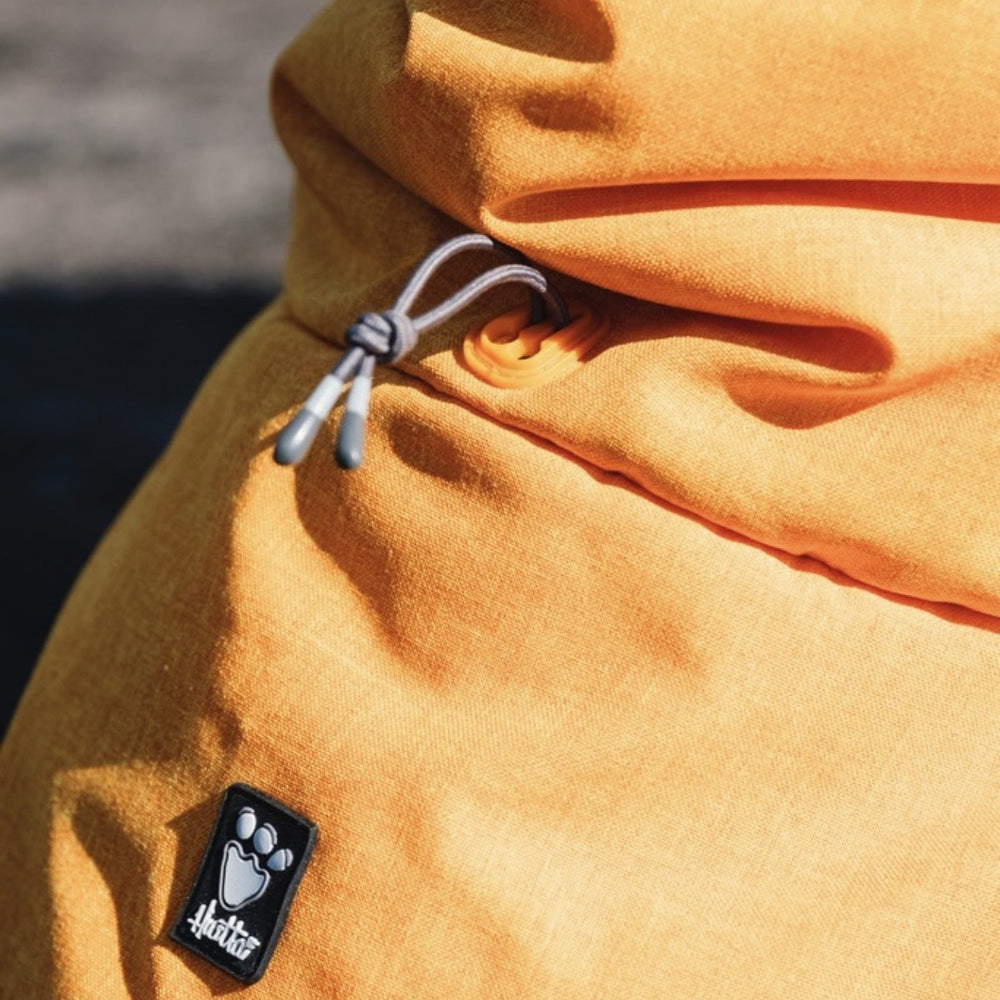 Orangefarbene Hundejacke mit Kordelzug und Pfotenabdruck-Etikett, ideal für Expeditionen und Outdoor-Abenteuer.