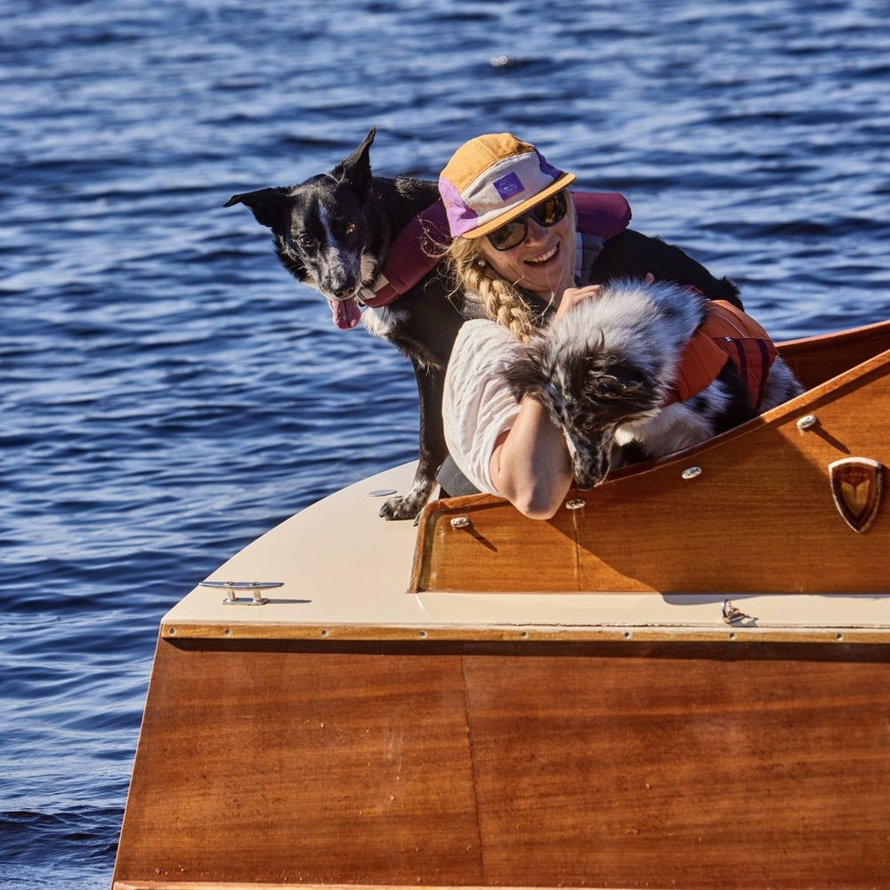 Person mit Sonnenhut und Hunden in Schwimmwesten auf Boot. Schwimmweste Life Savior ECO auf Wasser.