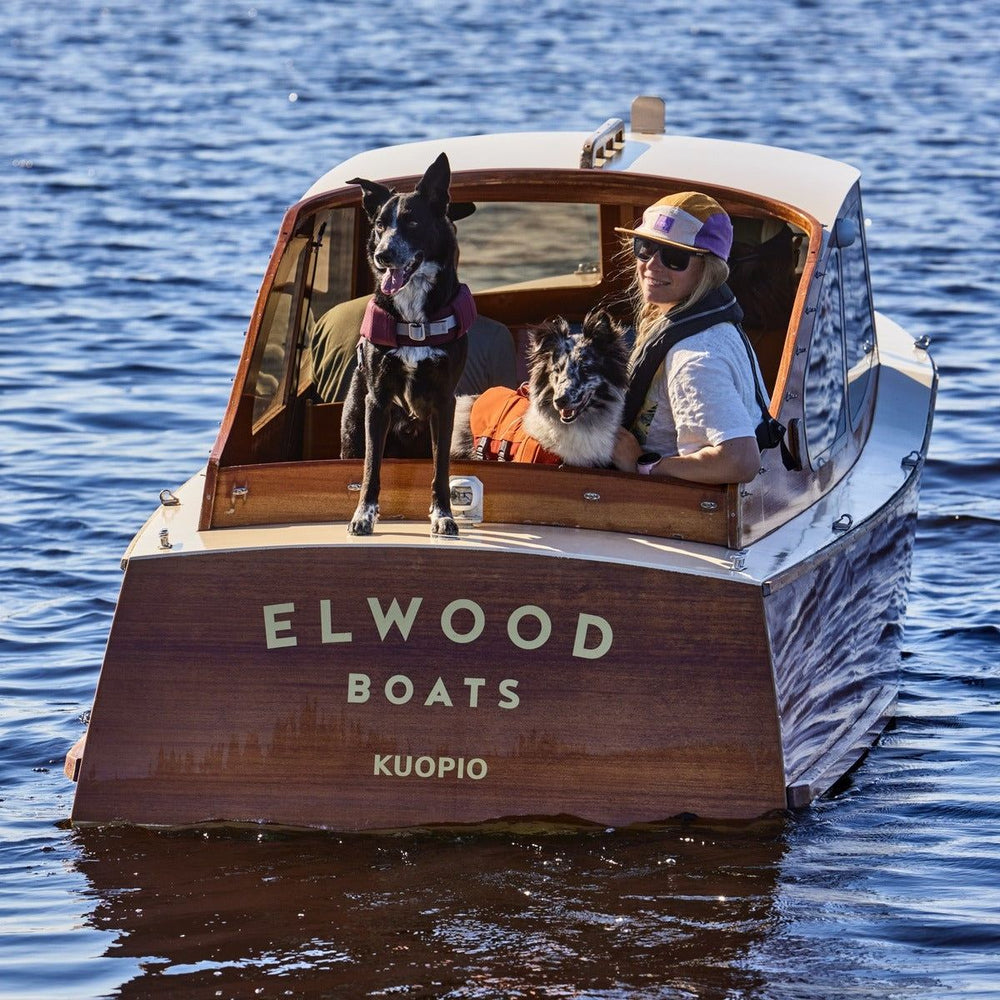Person und Hunde mit Schwimmweste Life Savior ECO auf Holzboot "Kuopio" von Elwood Boats auf sonnigem Gewässer.