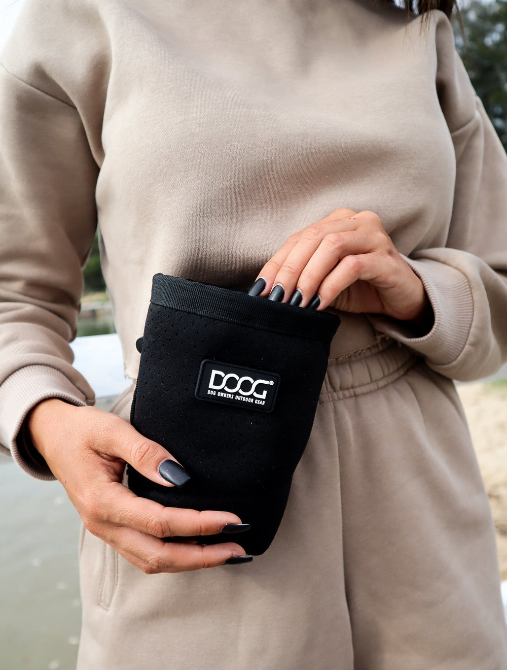 "Schnappschuss einer Person mit braunem Pullover, die den DOOG Neosport Treat & Training Pouch in schwarz hält."