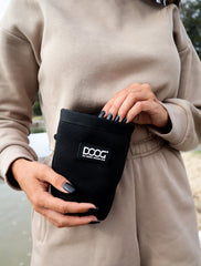 "Schnappschuss einer Person mit braunem Pullover, die den DOOG Neosport Treat & Training Pouch in schwarz hält."