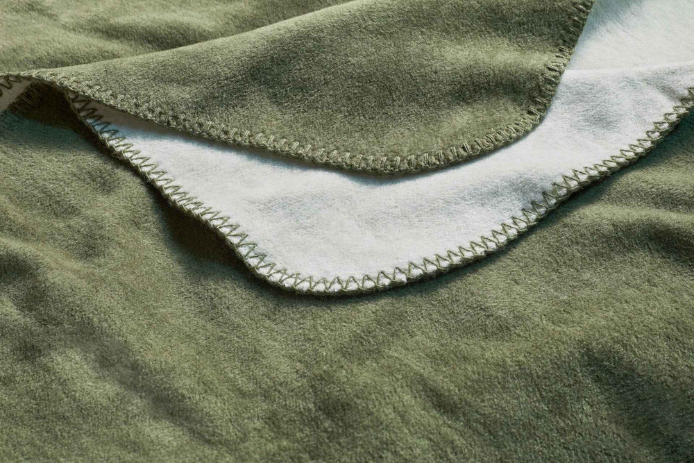"Stilvolle Wendedecke REVERSO in olivgrün und weiß, mit dekorativer Naht und weicher Textur - ideal für gemütliche Abende."