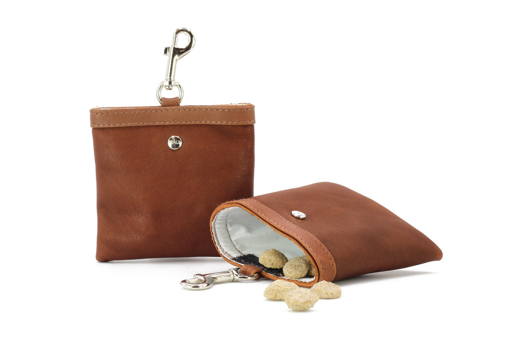 Brauner Leder-Leckerli-Beutel mit aufrecht stehendem Fach und Snacks, die aus dem geöffneten Fach herausragen.