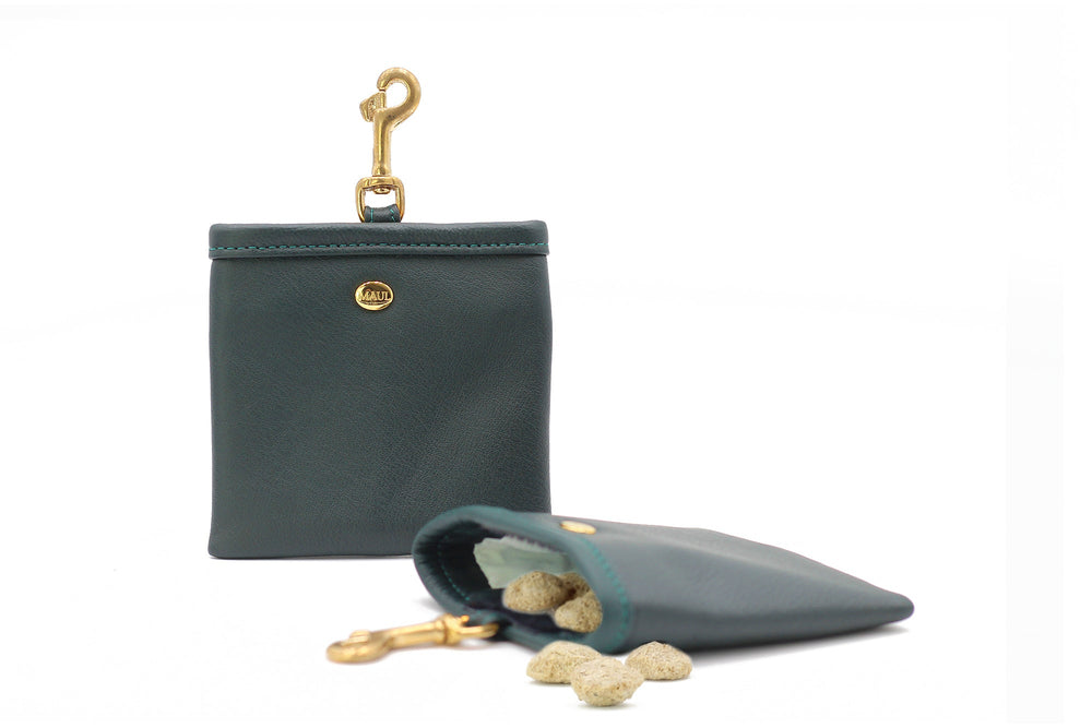 Kleines grünes Lederetui mit goldenen Clipverschluss, gefüllt mit beige Snacks, aufrecht stehend.