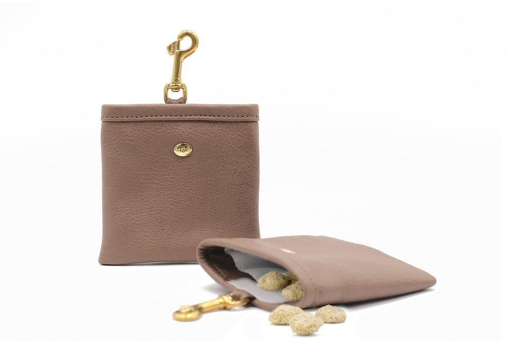 Braunes Leder-Portemonnaie mit goldenen Karabinerhaken, gefüllt mit Snacks und Leckerlis, teilweise herausfallend.