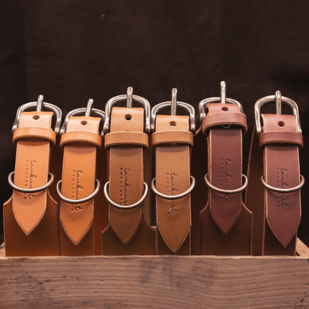 Reihe von eleganten Lederhalsbändern in Brauntönen mit Metallschnallen, stilvoll präsentiert in einem Holzbehälter.