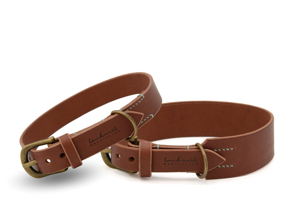 Zwei schlichte braune Lederarmbänder mit auffälliger Schnalle und kontrastierender Naht, eines mit "tanak" Logo.