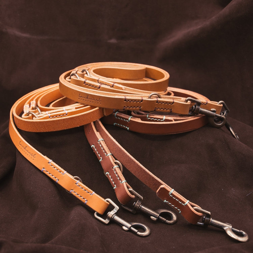 Verschiedene Lederhandstraps in Farbtönen mit Metallkarabiner, dekorativen Nähten auf dunklem Hintergrund.