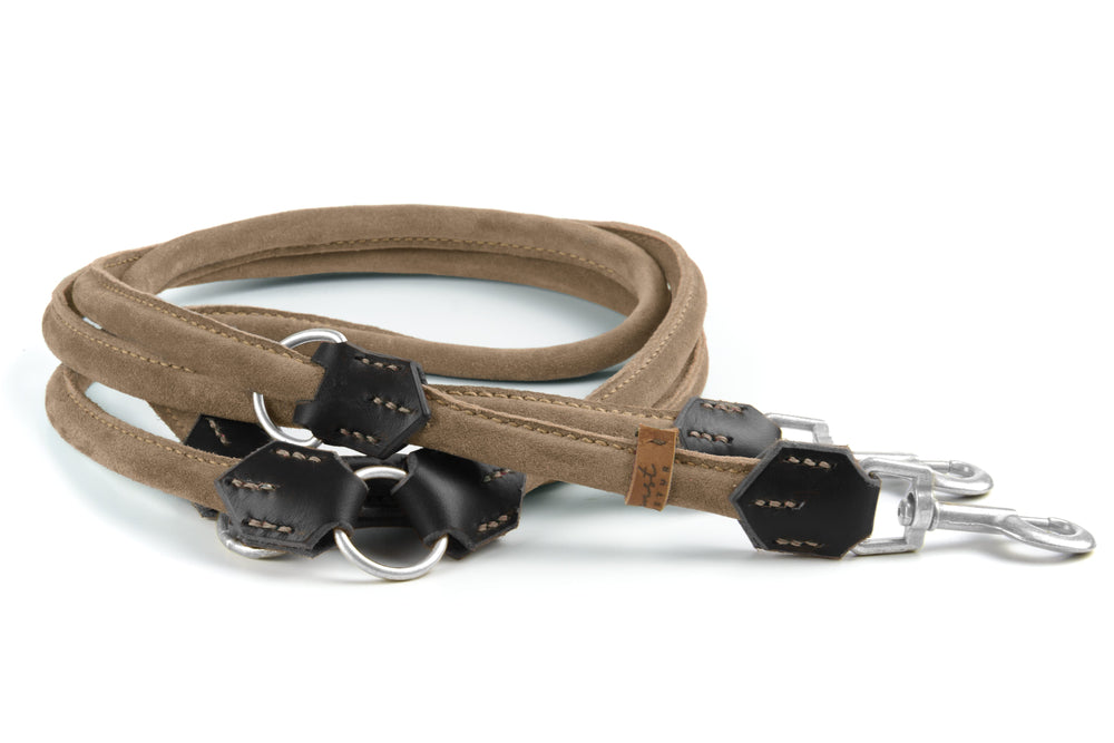 Beige Wildlederleine mit schwarzen Details und Karabinerhaken, auf weißer Oberfläche liegend. Ideal für stilbewusste Hundebesitzer.