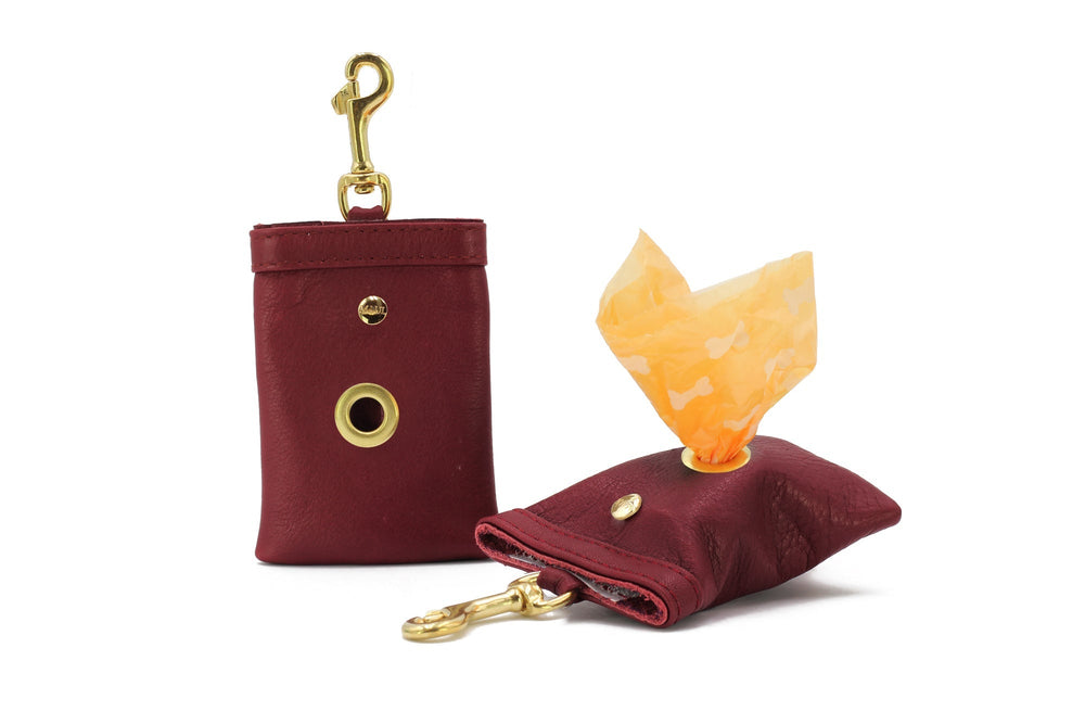 Hundekotbeutel-Halterung aus rotem Leder mit goldener Karabinerhaken und Öffnung für Beutel.