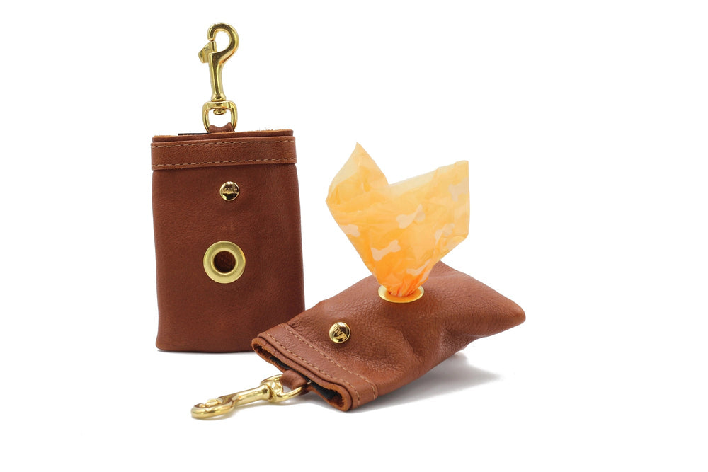 Brauner Leder-Taschenträger mit goldenen Beschlägen und orangefarbenem Müllbeutel, ideal für Hundebesitzer.