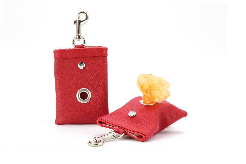 Roter Hundekotbeutelspender aus Kunstleder mit Karabiner und Druckknopföffnung, daneben eine Rolle Hundekotbeutel.