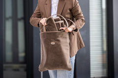 Braune Hundereisedecke für Dackel in samtiger Tasche, gehalten von einer elegant gekleideten Person.