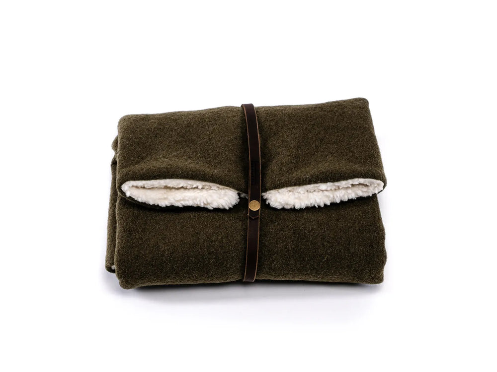 "Reisedecke Forest in olivgrün mit weißer, pelzähnlicher Innenseite, zusammengebunden mit Lederband und Druckknopf."